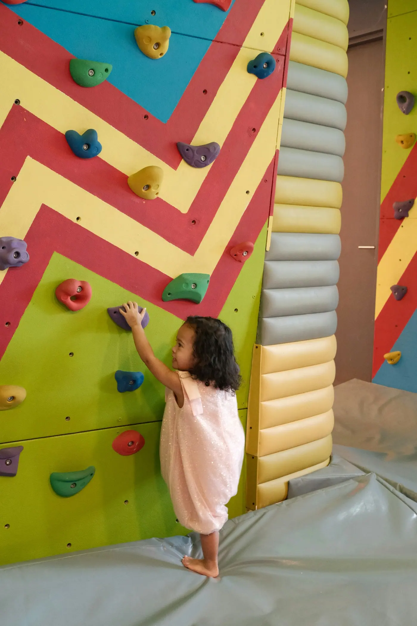A small child climbing a wall covered in colourful holds